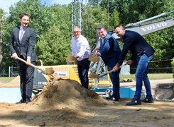 Man sieht viert Männer in Anzug, die mit Spaten Sand in die Luft werfen.