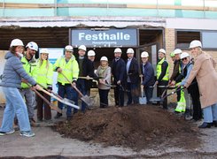 Quelle: Gemeinde Sandhausen Das Bild zeigt einen Spatenstich. Eine Gruppe mit Baustellenhelml und Spaten sticht in einen Sandhaufen.