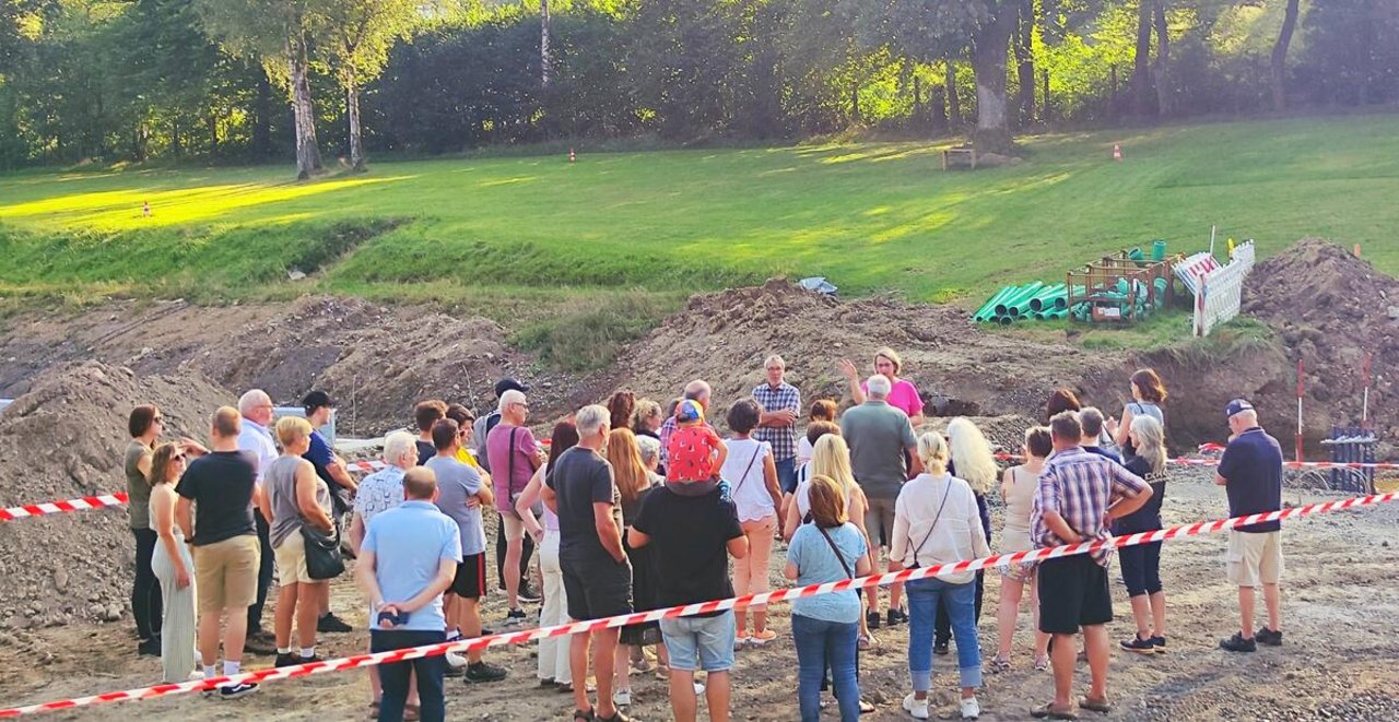 Man sieht eine Gruppe Menschen, die zwischen Absperrbändern in einer Grube stehen.