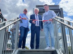 Quelle: Gemeinde Augustdorf Das Bild zeigt drei Männer auf der oberen Schwelle einer Außentreppe, einer von ihnen schneidet ein Band durch.