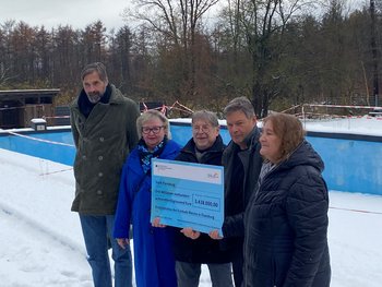 Man sieht fünf Personen in einem verschneiten Freibad. die einen großen Spendenscheck halten. 