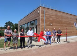 Quelle: Kunigundengemeinde Kaufungen Acht Personen stehen vor einem Gebäude mit Holzfassade und durchtrennen gemeinsam ein rotes Band mit mehreren Scheren.