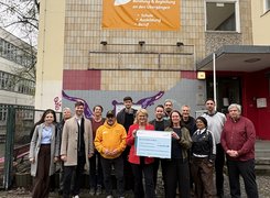 Quelle: BMWSB/Tonya Yotova Eine Gruppe Menschen steht vor einem Gebäude und posiert für ein Foto. Zwei Personen in der Mitte halten einen Förderscheck in der Hand.