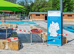 Quelle: Stadt Wuppertal/GMW Foto: Frank Buetz Ein Freibadgelände mit Roll-Up, Absperrung, Rettungsring und Sonnenschirm.