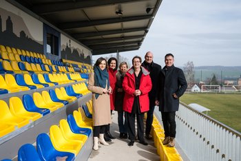 Eine Gruppe Menschen stehe auf einer Tribüne eines Stadions.