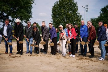 Man sieht eine Gruppe Menschen, die einen Spatenstich vollziehen. 