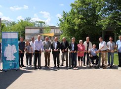 Quelle: S.Dettmer/LK Helmstedt Das Bild zeigt eine Gruppe von Menschen vor einem Zeremonieband. Die Menschen sind kurz davor, dieses zu zerschneiden.