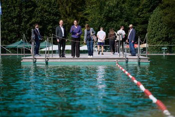 Eine Gruppe Menschen steht am Rand eines Schwimmerbeckens in einem Freibad.