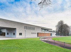 Quelle: Architektur Büro Müntinga Schimmelpfeng Das Bild zeigt einen Rasenplatz mit Laufbahn und einem neuen Gebäude.